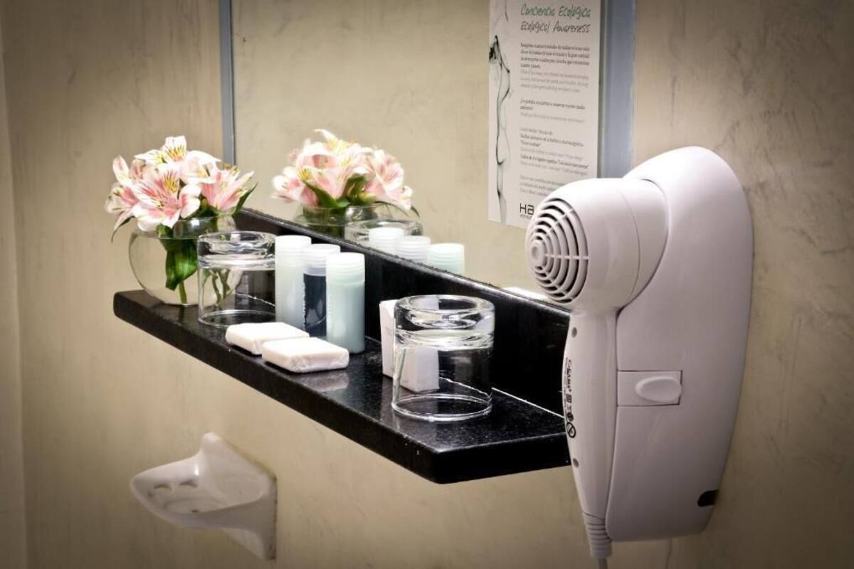 A bathroom with a hairdryer on a black countertop, a vase with flowers, and a mirror.