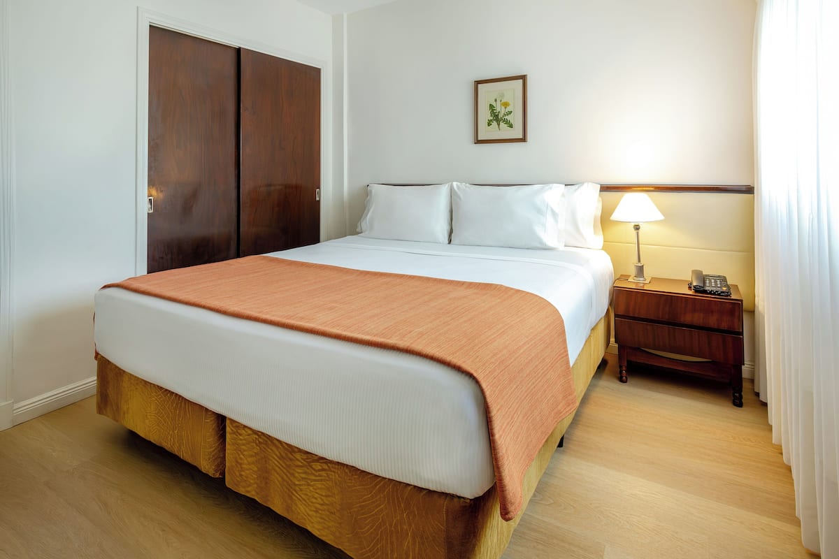 A hotel room with a bed, a nightstand, a lamp, and a door.