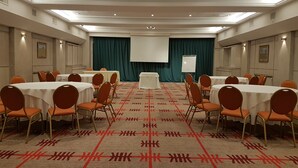 Un salón de conferencias con mesas, sillas, una pantalla de proyector y una pizarra.