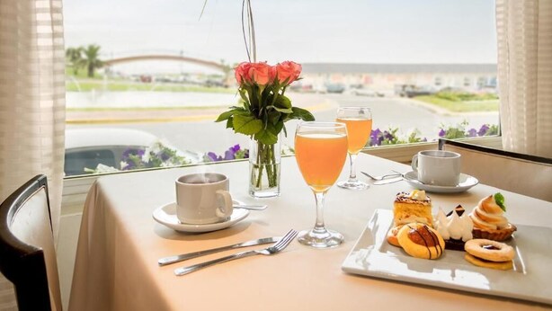 Una mesa con alimentos para el desayuno, un jarrón con flores y vistas a un puente y una carretera.