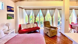 A bedroom with a bed, a red sofa, a chair, and large windows with curtains. - Wonderful Mountain Views (Escobal)