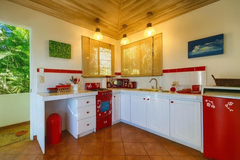 A kitchen with white cabinets, red accents, and a wooden ceiling.