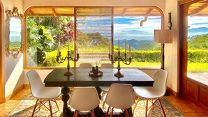 A dining area with a table and chairs, large windows with a view of greenery and mountains, and a wooden ceiling. - Wonderful Mountain Views (Escobal)