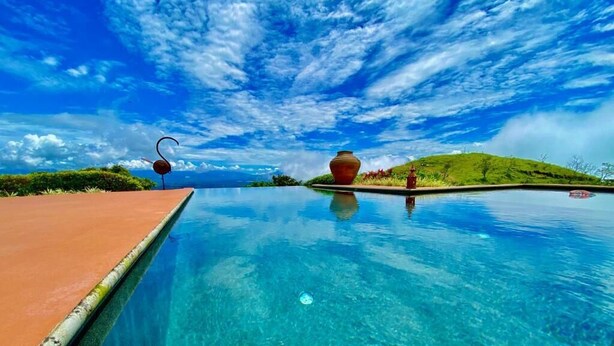 A clear blue pool with a view of a green hill and a red pot in the background. - Wonderful Mountain Views (Escobal)