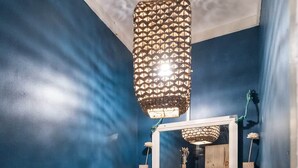 Un baño con pared azul, tocador de madera, lavamanos blanco, espejo y lámpara colgante.