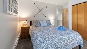 A bedroom with a patterned bedspread, a wooden dresser, two bedside lamps, and a wooden wardrobe. - Tenney 4BR : Foliage, Hiking & Lakes : Wood Fireplace (Plymouth)