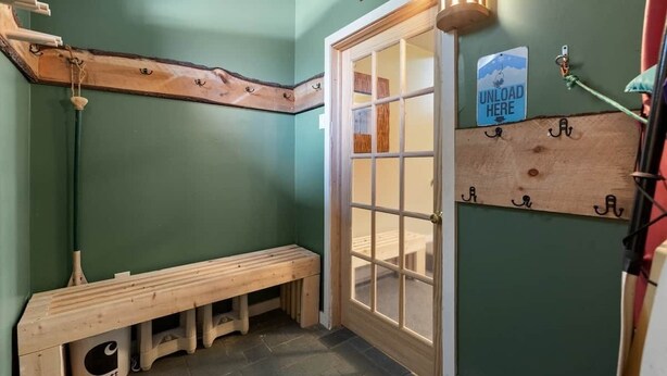 Un rincón de una habitación con un banco de madera, una puerta con panel de vidrio y un cartel que dice 'UNLOAD HERE'.