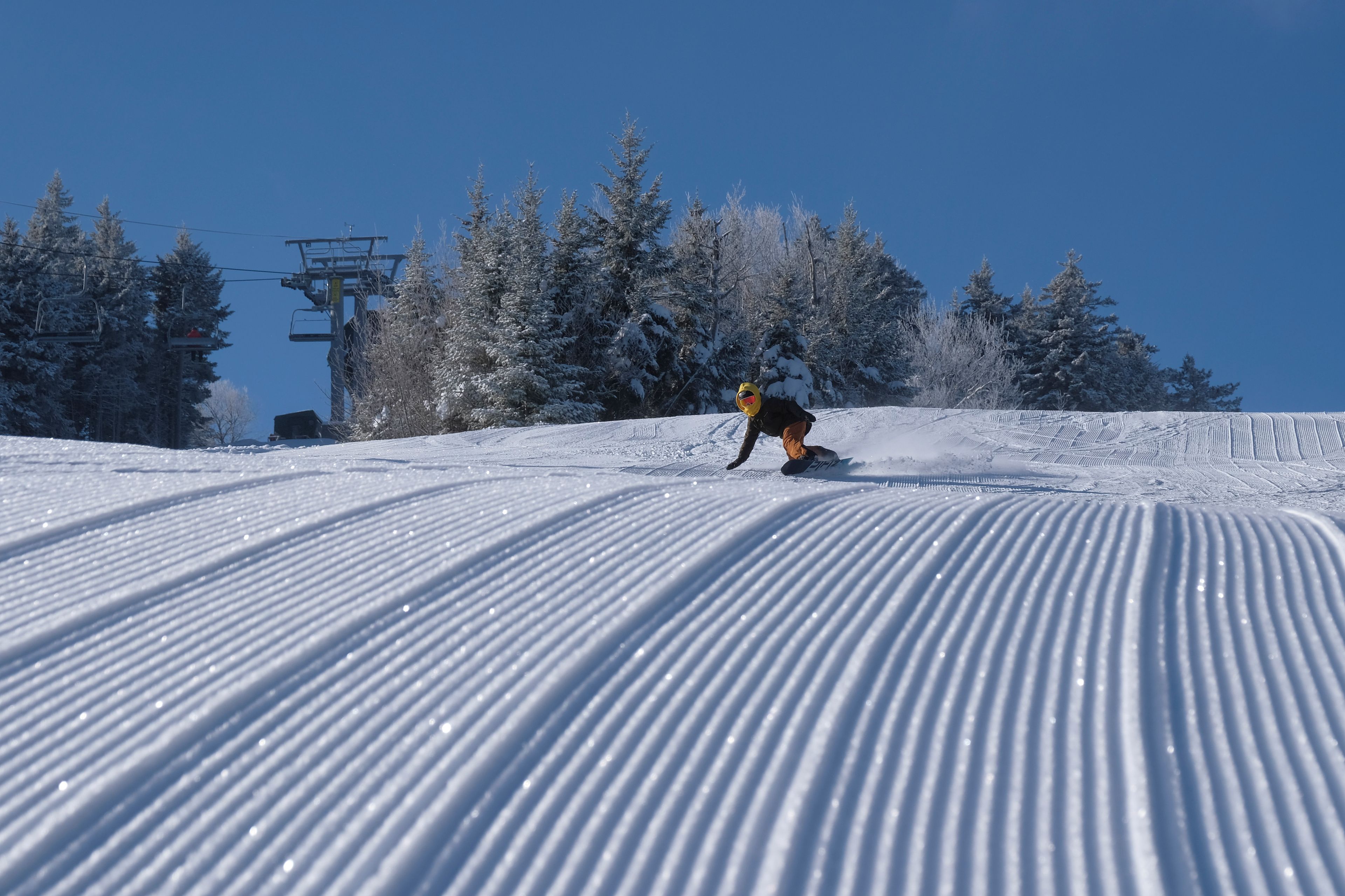 Un snowboardeur dévale une pente enneigée, avec un télésiège en arrière-plan.