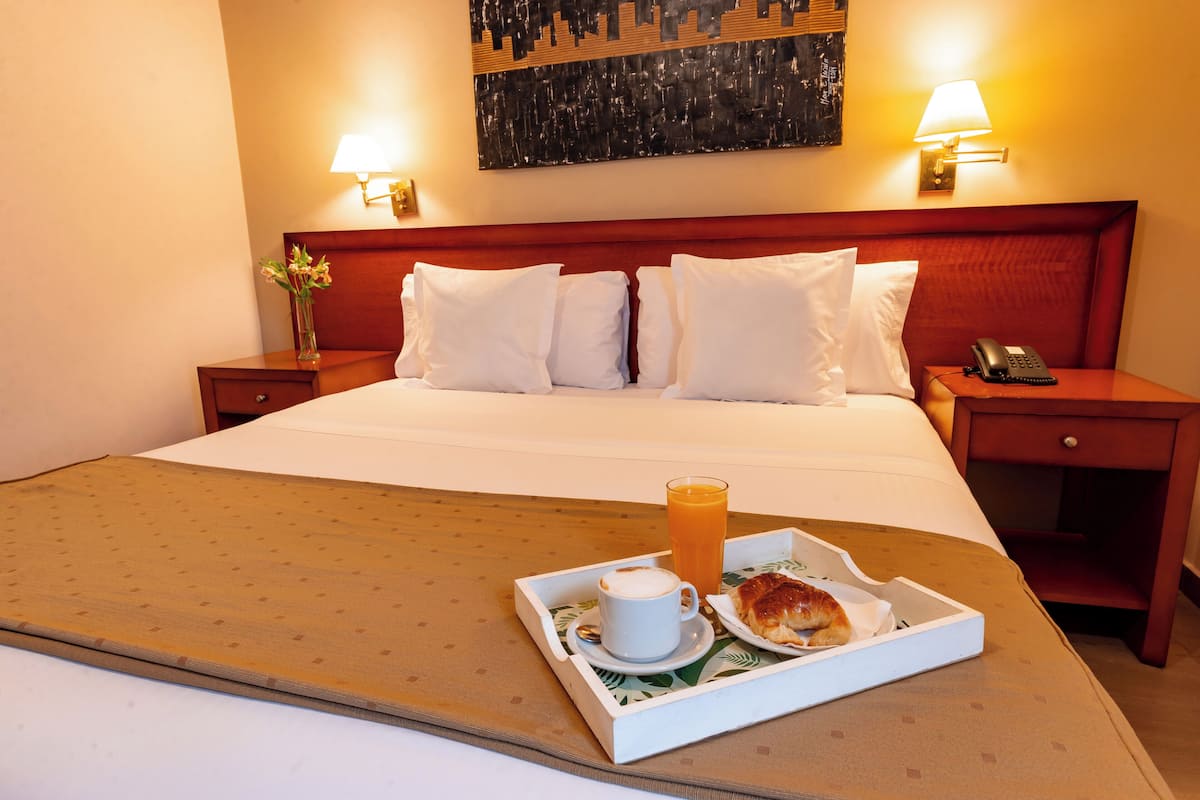 Une chambre d’hôtel avec un lit bien fait, une table de chevet avec une lampe, une petite table avec un téléphone et un plateau contenant des articles pour le petit-déjeuner.