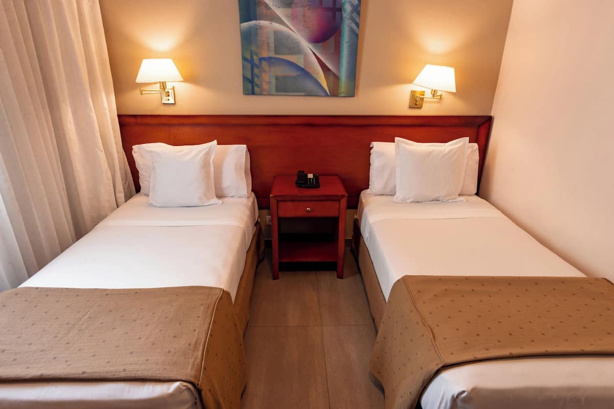 Une chambre d’hôtel avec deux lits, une table de chevet, un téléphone et un tableau au mur.