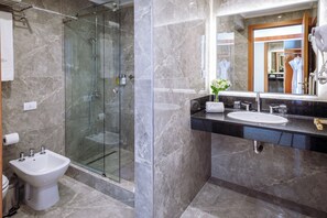 Un baño moderno con ducha de vidrio, un bidé, un lavabo con espejo y un perchero para toallas.