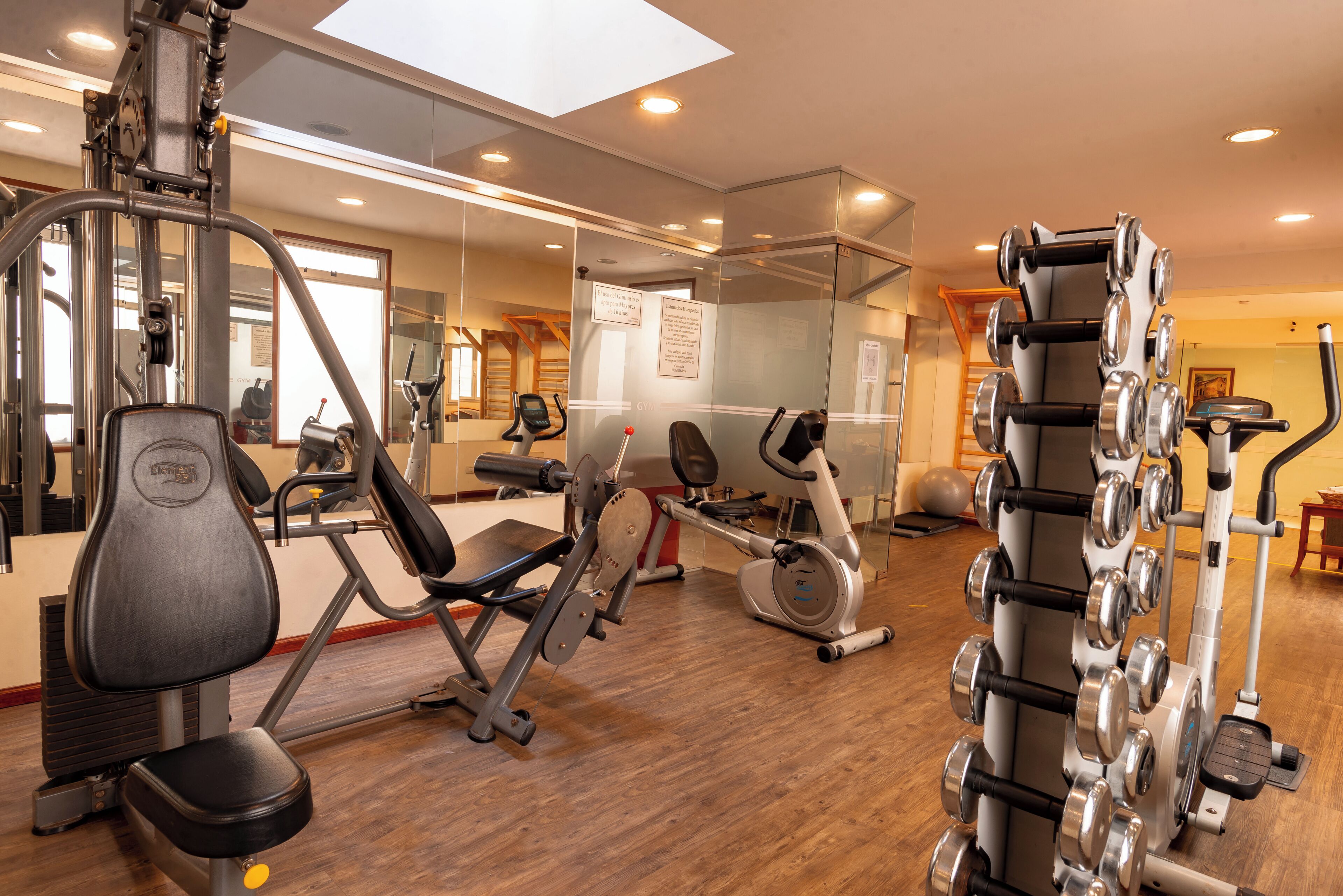 Un gimnasio con equipo de ejercicio, un espejo y piso de madera.