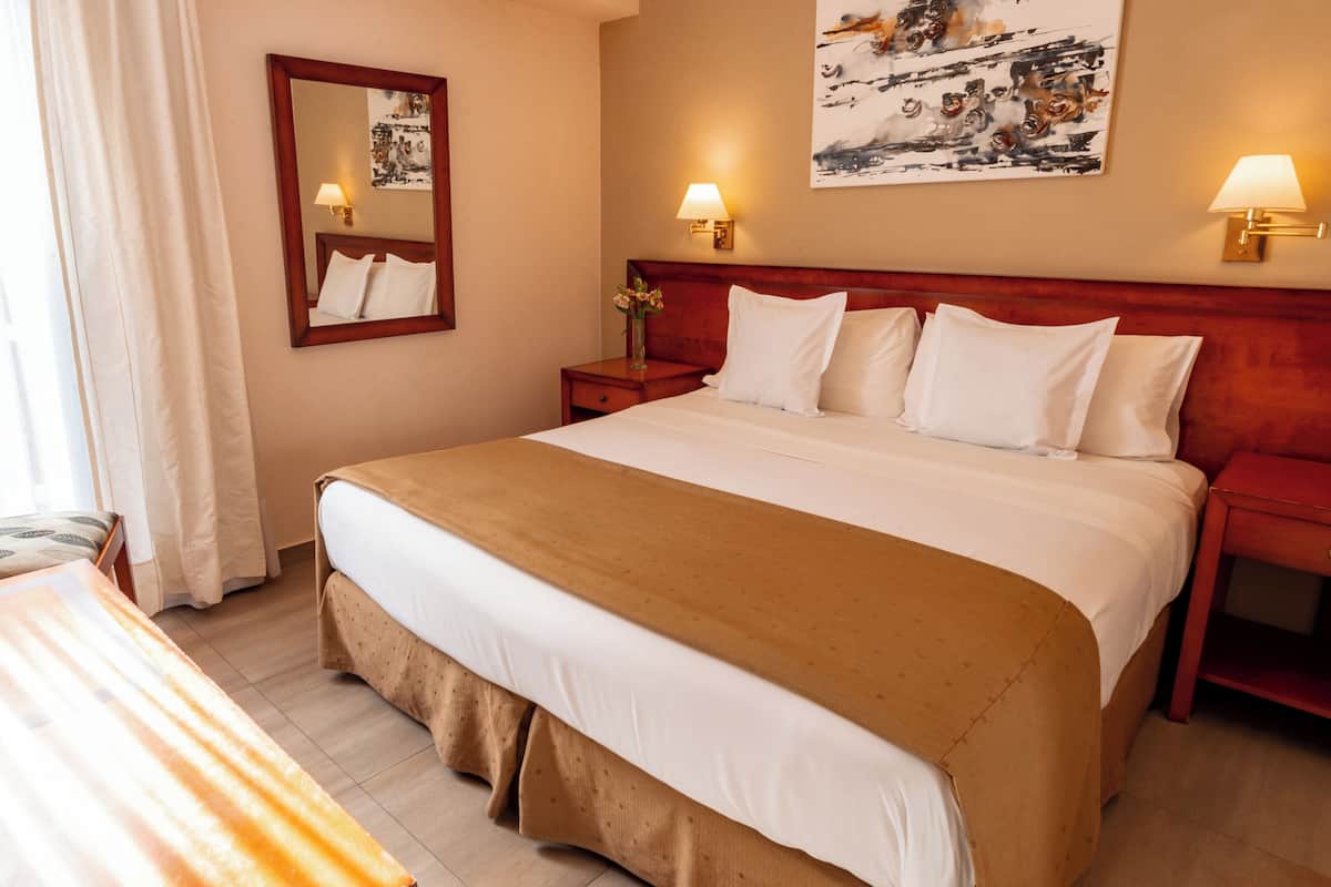 Une chambre d’hôtel avec un grand lit, une table de chevet avec une lampe, un miroir et un tableau au mur.