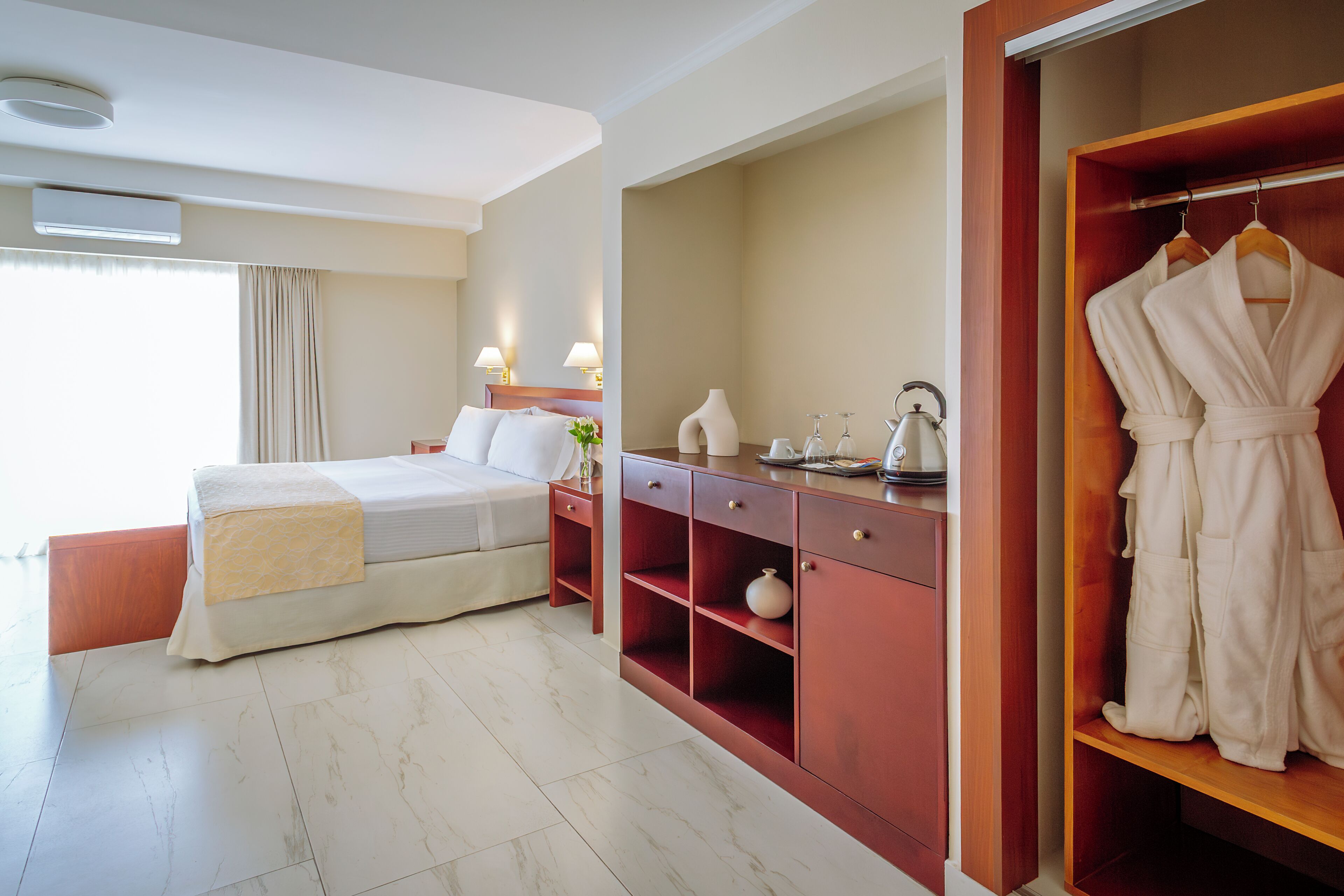 A hotel room with a bed, a wooden wardrobe, a bedside table, and a mirror.