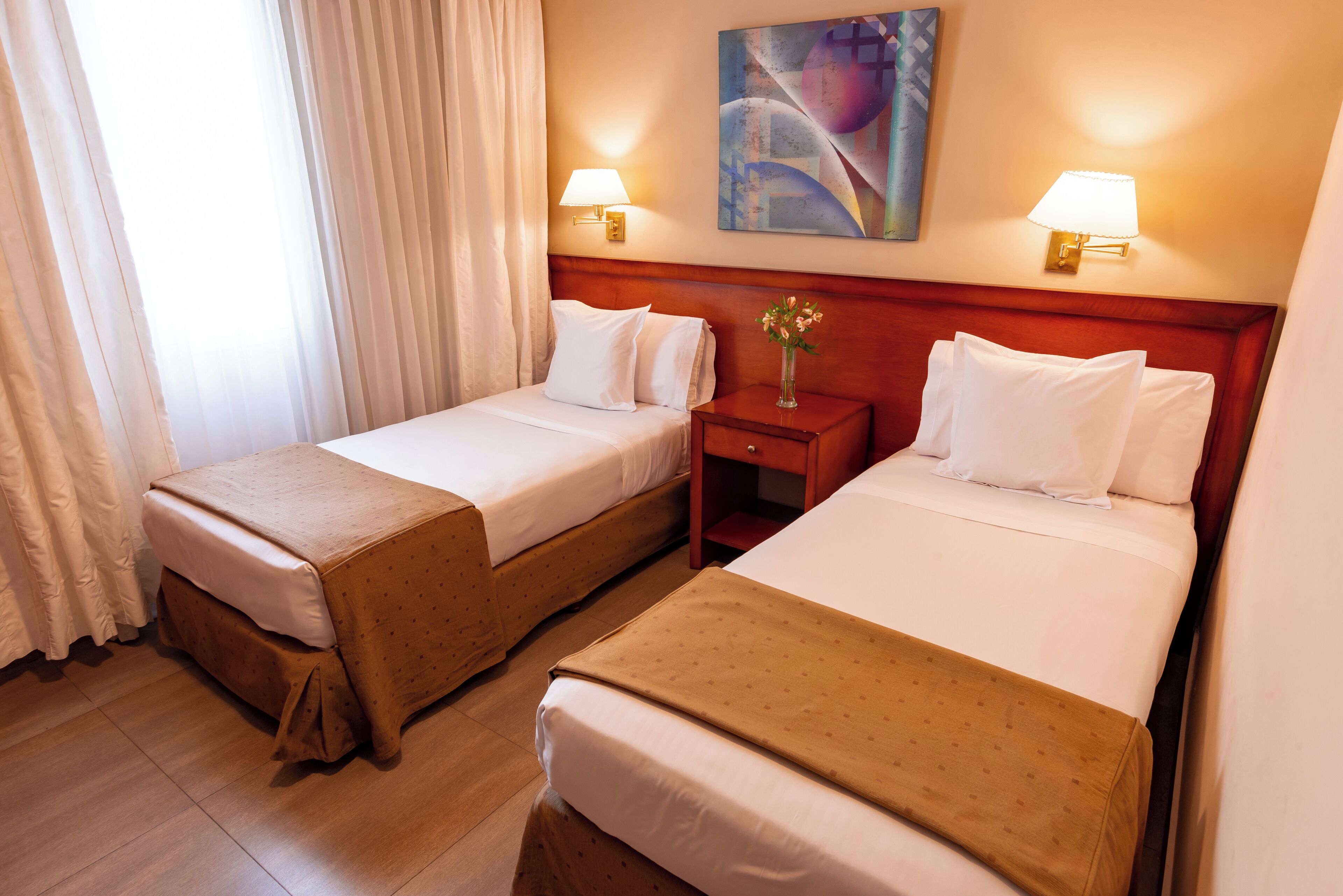 Habitación de hotel con dos camas, una mesita de noche, una lámpara y un cuadro en la pared.