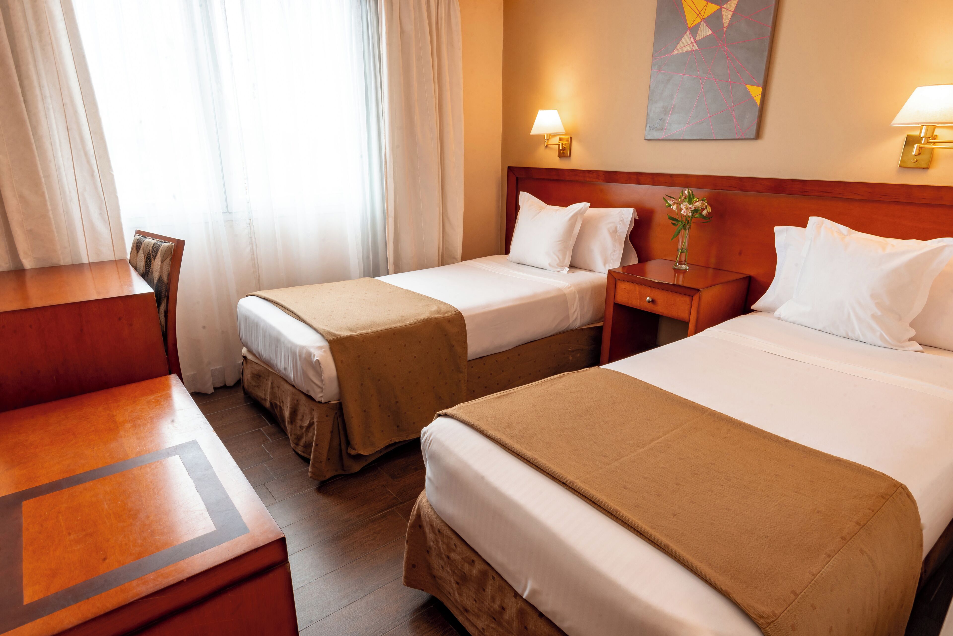 Quarto de hotel com duas camas, uma escrivaninha e uma cadeira.