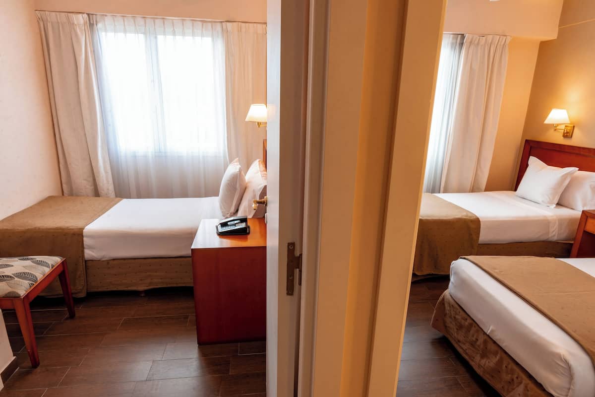 Une chambre d’hôtel avec deux lits, un bureau, une chaise et une fenêtre avec des rideaux.
