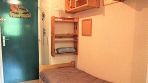 Une petite pièce, de taille modeste, comprenant un lit simple, une étagère en bois et une porte.