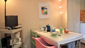 Un petit coin repas avec une table dressée pour deux personnes, un téléviseur posé sur un meuble et une machine à café.
