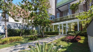 A modern building with a glass entrance, surrounded by well-maintained greenery and a clear pathway. - Studio with Pool and Garage – 7 min from Allianz (São Paulo)