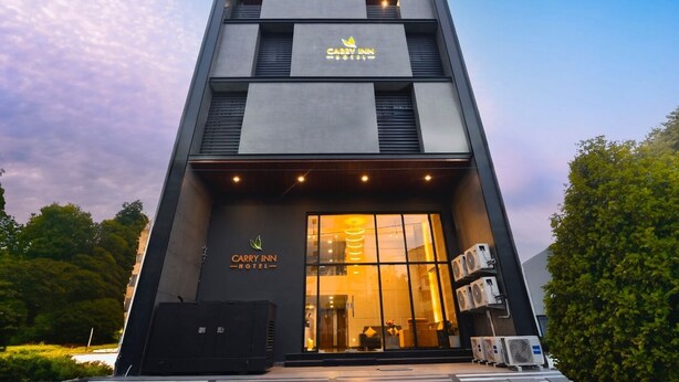 Una entrada de hotel moderna con un gran ventanal, un letrero que dice "Carry Inn Hotel" y unidades de aire acondicionado a la derecha.