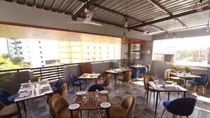 Un restaurante en la azotea con mesas y sillas, asientos al aire libre y vistas a edificios y zonas verdes.