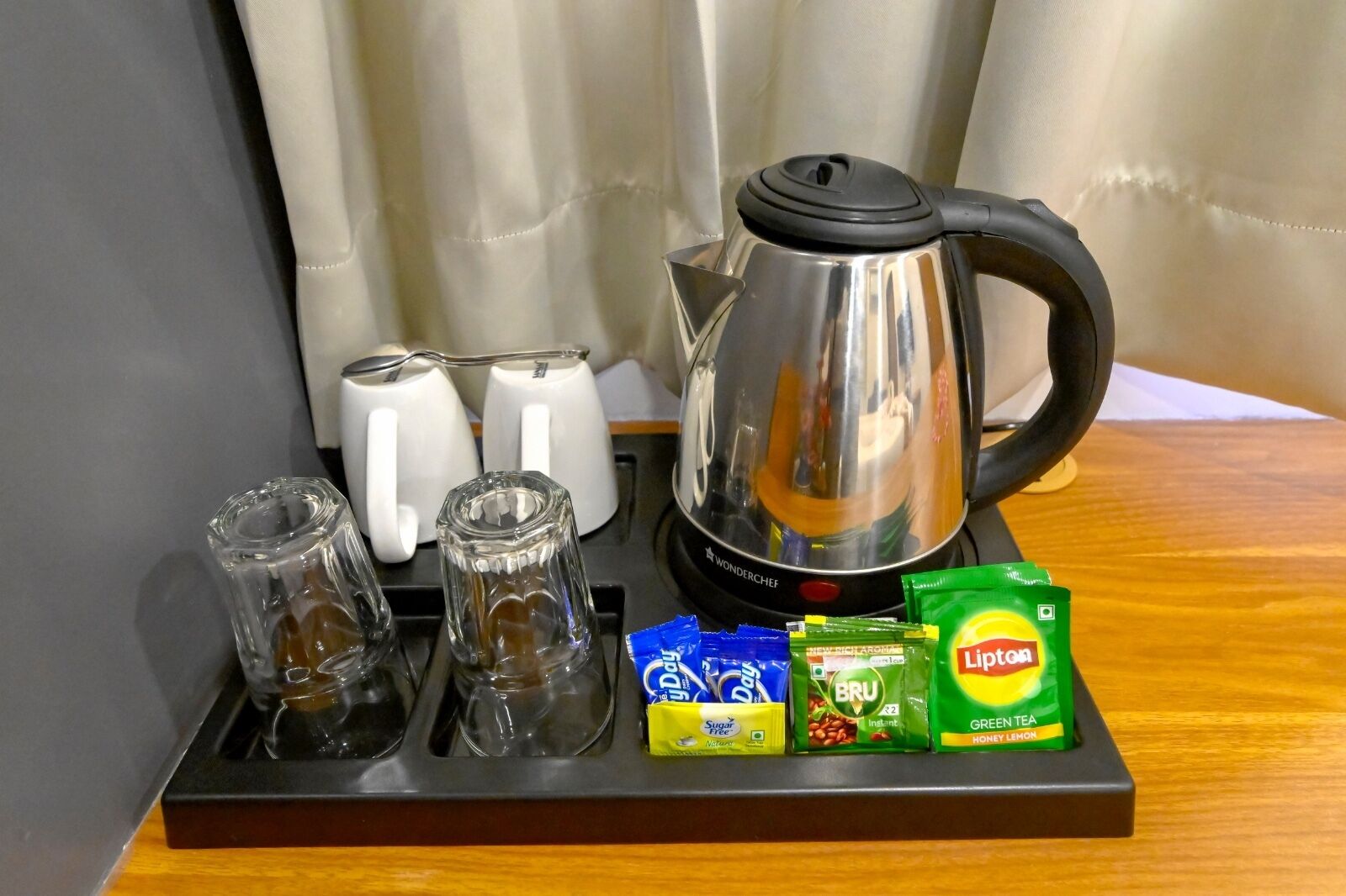 A kitchen area with a stainless steel kettle, two white mugs, and a tray with Lipton tea bags and a box of BRU instant coffee.