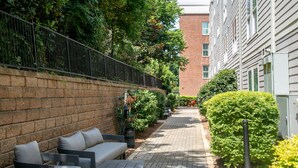 A paved pathway lined with outdoor seating, a brick wall, and a hedge. - The George, 3BR Home by Velvet Ditch Villas (Oxford)