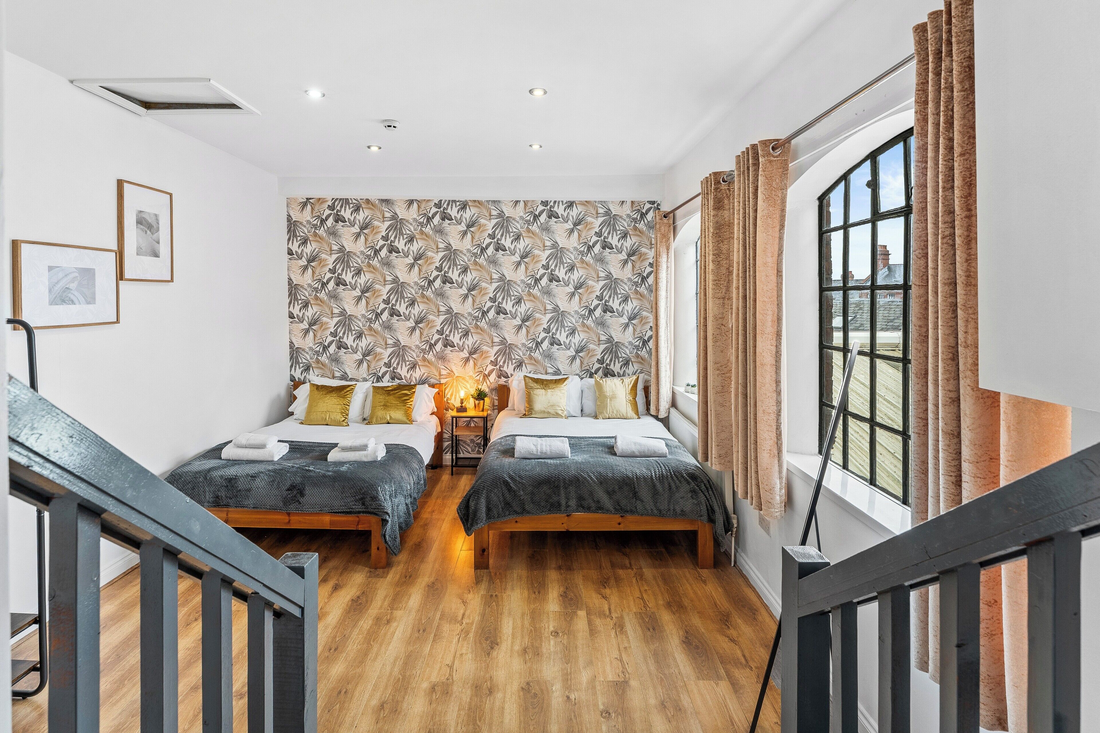 Une chambre avec deux lits, un mur décoré de motifs, une fenêtre avec des rideaux et un plancher en bois.