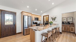 A modern kitchen with a central island, wooden cabinets, stainless steel appliances, and a large window. - Lake House for 14! Fire Pit + Game Room (New Lisbon)