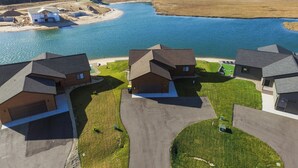 A residential area with houses near a body of water, featuring a driveway and a well-maintained lawn. - Lake House for 14! Fire Pit + Game Room (New Lisbon)