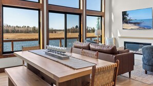 A spacious living room with a large wooden table, leather sofa, and a fireplace. - Lake House for 14! Fire Pit + Game Room (New Lisbon)