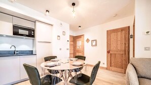 A compact kitchen with modern appliances, a dining area with a round table and chairs, and a wooden door. - 140m from ski lifts, 1st floor, balcony, tv, 33m², Morzine (Morzine)