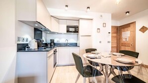 A modern kitchen with white cabinets, a built-in oven, and a dining area with a round table and chairs. - 140m from ski lifts, 1st floor, balcony, tv, 33m², Morzine (Morzine)