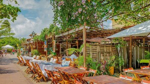 Un restaurant en plein air avec des tables et des chaises en bois, entouré de verdure et agrémenté d’une pergola en bois.