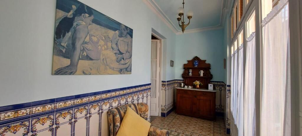 Een hal met betegelde vloer, een schilderij aan de muur, een houten kast en een deur naar een andere kamer.