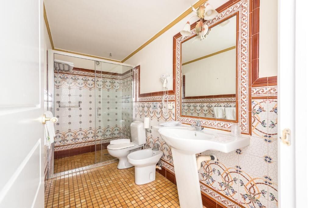 Casa de banho com chuveiro, duas sanitas, lavatório e espelho.