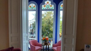 A room with a bay window featuring stained glass, a small table with a vase of flowers, and two patterned chairs. - Hotel Noucentista (Sitges)