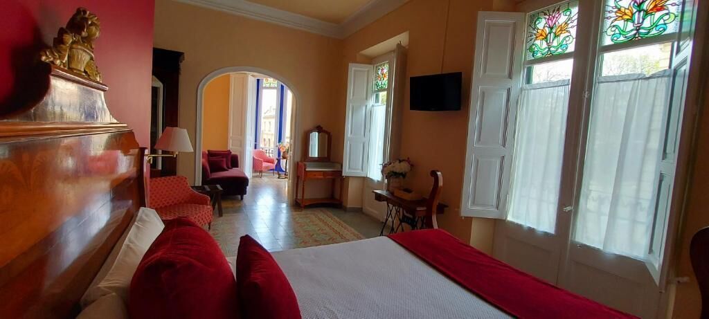 Habitación de hotel con cama, escritorio, silla, televisión y ventana con vitral.