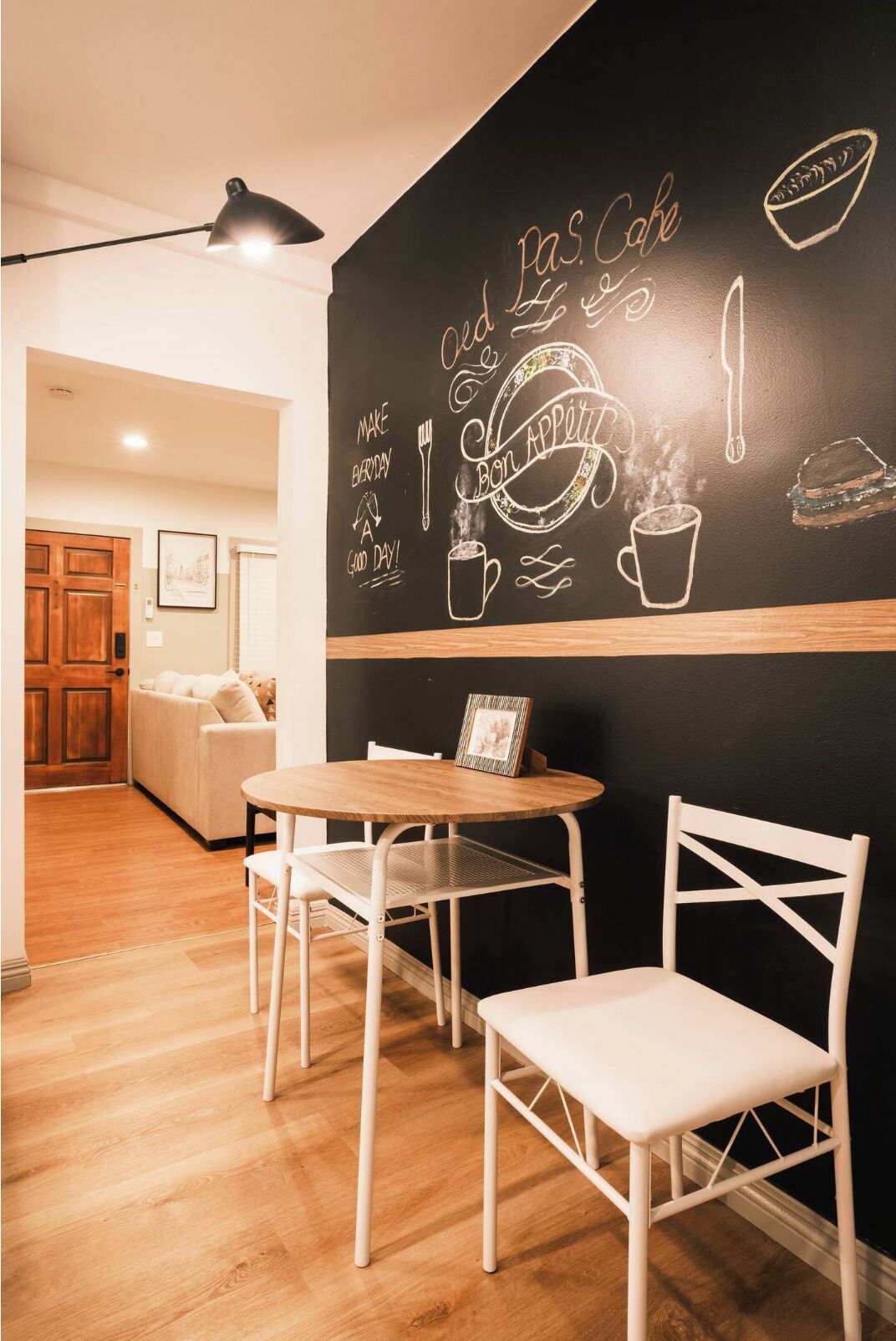 Un rincón comedor acogedor con una pared de pizarra decorada con dibujos hechos a tiza de comida y utensilios, una mesa redonda de madera y sillas blancas.