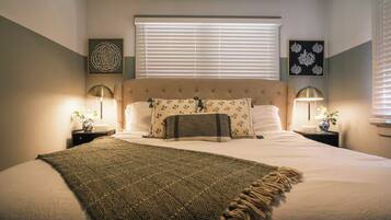 Un dormitorio ordenado con una cama grande, dos mesitas de noche con lámparas y obras de arte en las paredes.