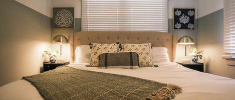 Un dormitorio ordenado con una cama grande, dos mesitas de noche con lámparas y obras de arte en las paredes.