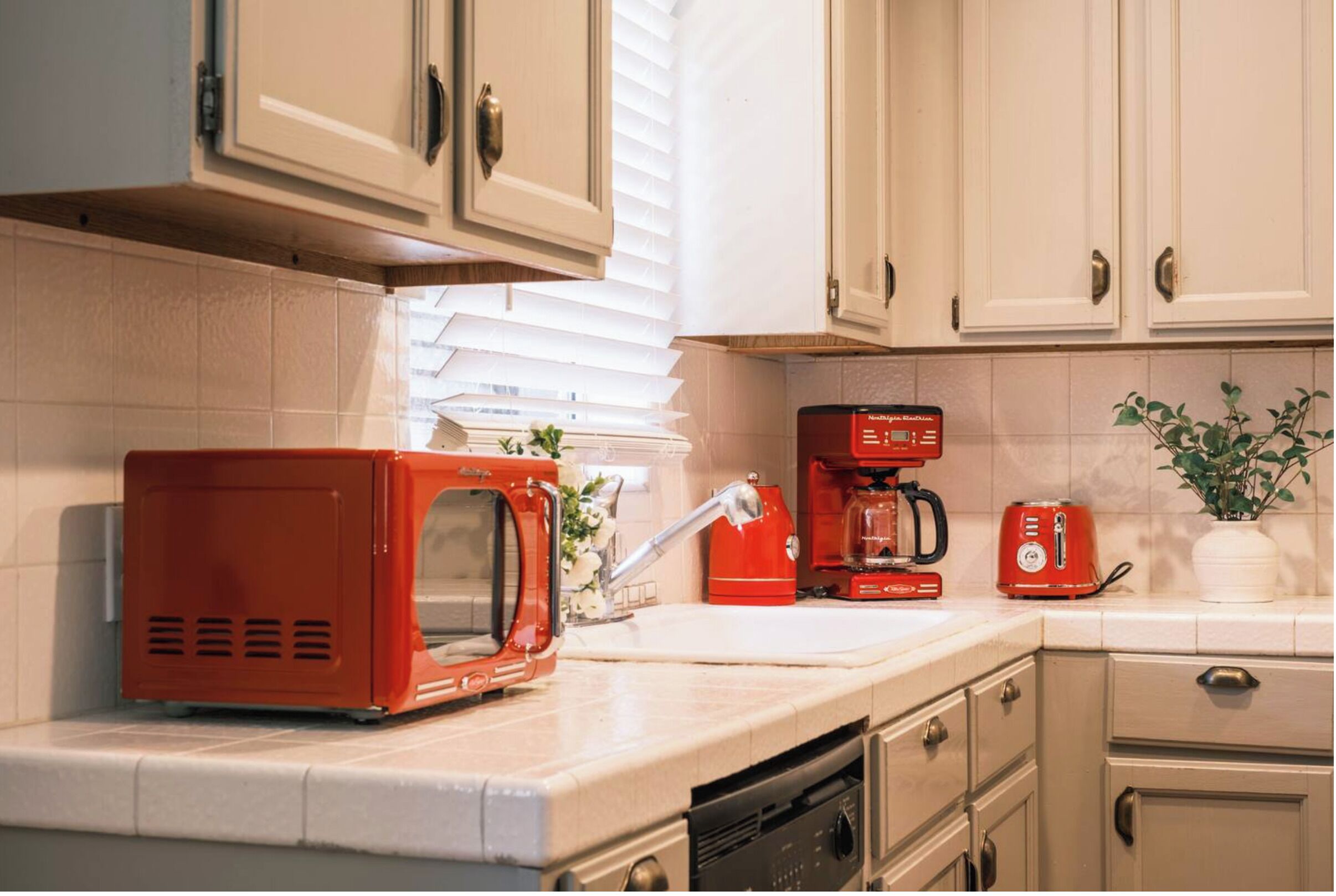 Una cocina con armarios blancos, un microondas rojo, una cafetera roja y un tostador.