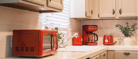 Una cocina con armarios blancos, un microondas rojo, una cafetera roja y un tostador.