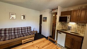 A compact living space with a sofa, a wooden table, a kitchenette with a microwave and sink, and a door leading to another room. - Ski-in/ski-out & foot of the slopes, 2nd floor, balcony, tv, 17m², Auris en Oisans (Auris)