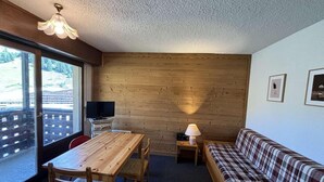 A room with a wooden table, a sofa, a TV, and a lamp. - Ski-in/ski-out & foot of the slopes, 2nd floor, balcony, tv, 17m², Auris en Oisans (Auris)