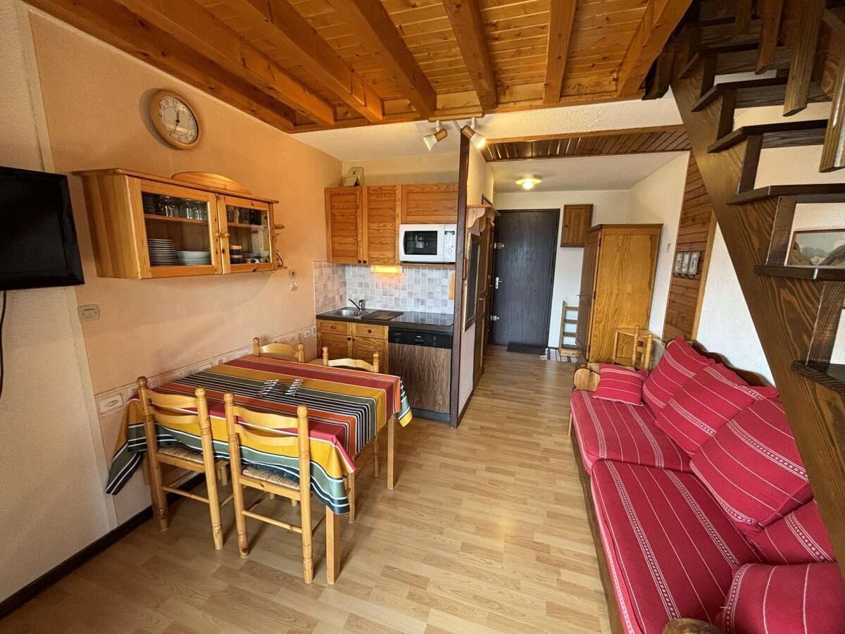 A cozy interior with a dining table, chairs, a sofa, wooden cabinets, a microwave, and a clock on the wall.