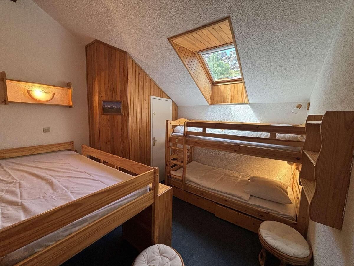 Ein kleines Zimmer mit zwei Etagenbetten, einem kleinen Hocker, einem Holzschrank und einem Oberlicht.
