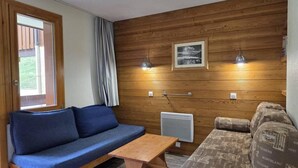 Ett mysigt rum med en blå soffa, ett träbord och en mönstrad soffa.