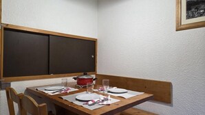 En matplats med ett träbord dukat för två personer, en röd kruka på bordet och en inramad tavla på väggen.